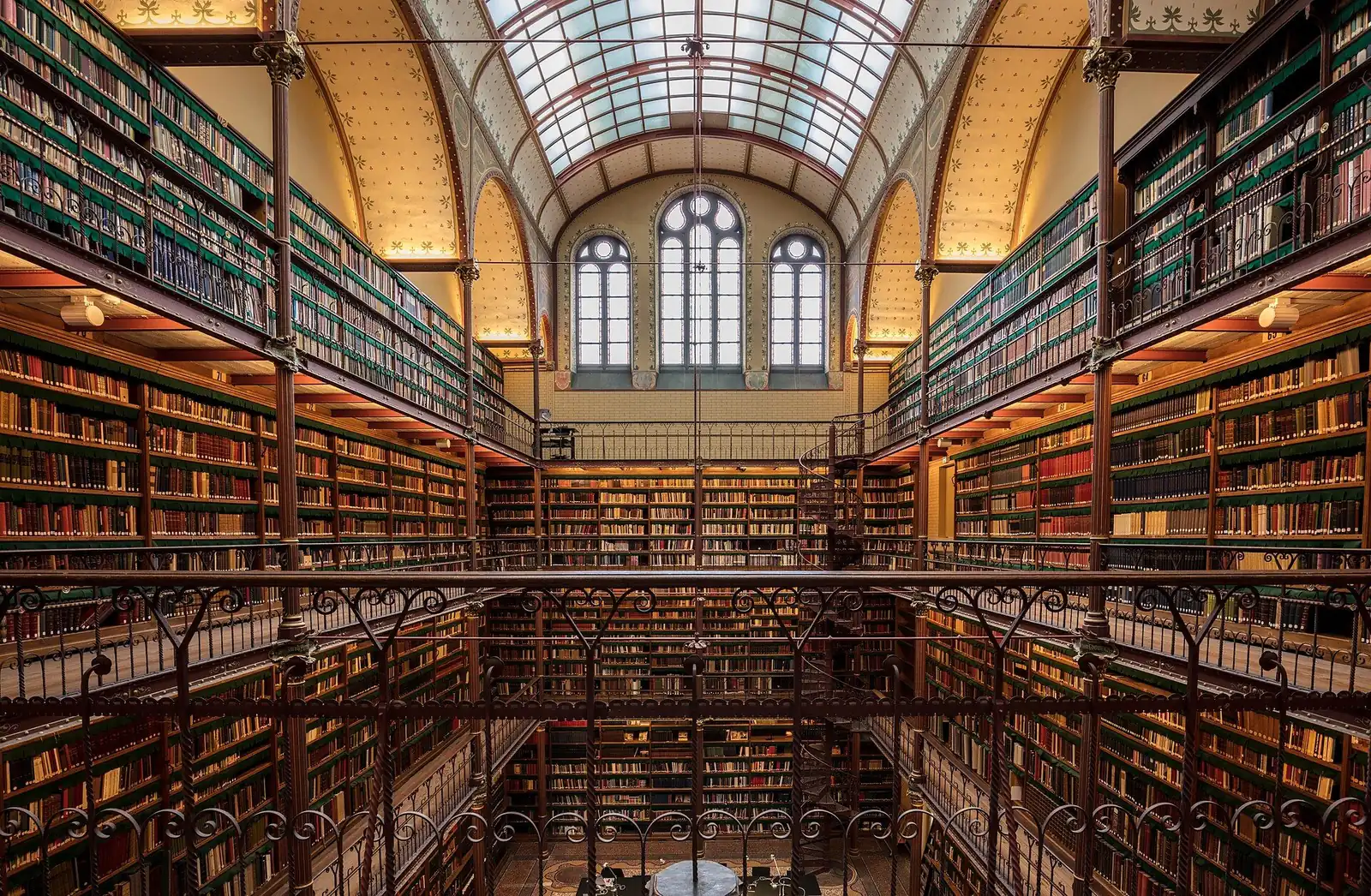 Bibliothèque monumentale sur plusieurs galeries en fer forgé sous une verrière