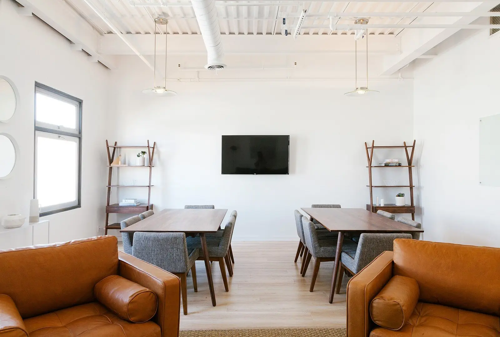 Espace de réunion clair avec fauteuils en cuir fauve, tables en bois et étagères